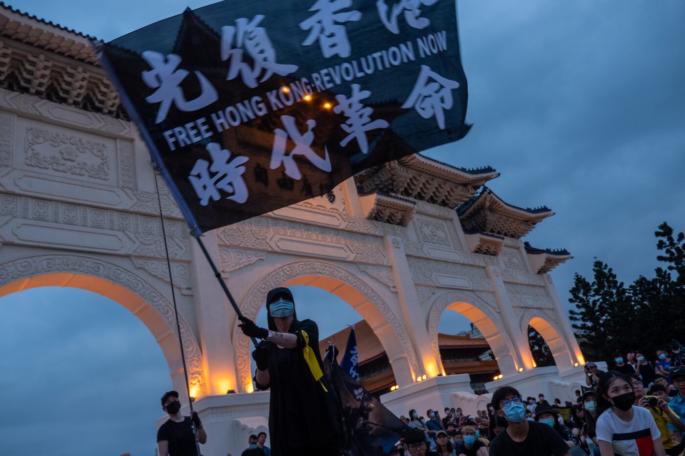 A protester holds a large black Free Hong Kong flag at Liberty Square in Taipei at dusk
